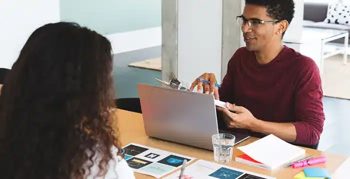 A man and a woman sitting at a table looking at a laptop.